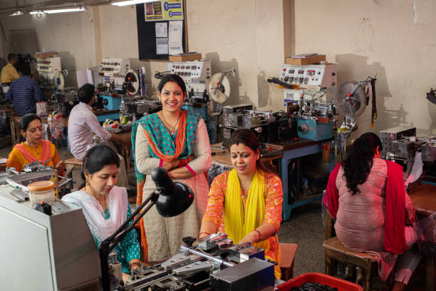 High angle view of confident female coworkers looking at camera while operating fabric cutting and printing machineries at textile factory representing women empowerment